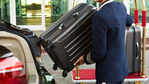Bellboy dỡ hành lý từ trên xe taxi xuống và đưa lên xe đẩy